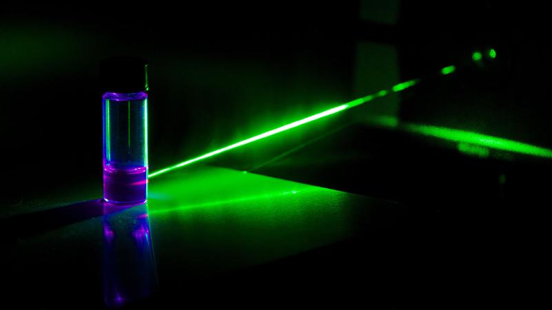 Green laser striking vial of liquid, with beam changing colour as it passes through.